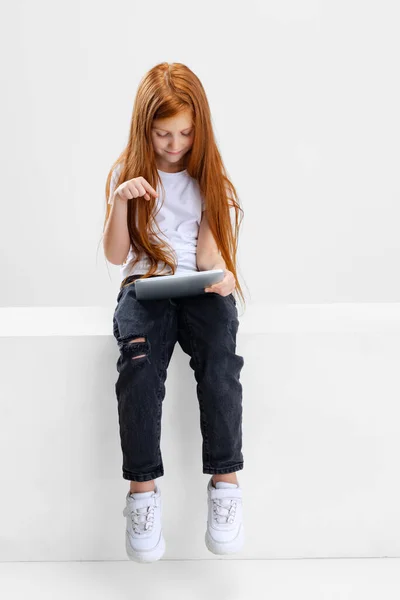 Portrait of little Caucasian girl, child typing ot playing on tablet isolated over white studio background. — Stock Photo, Image
