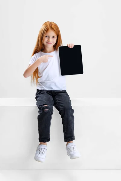 Retrato de una niña preescolar apuntando a una tableta aislada sobre fondo blanco del estudio. Dispositivo moderno — Foto de Stock