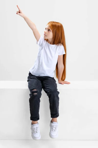 女の子の肖像、白い背景の上に隔離されたどこかを指すカジュアルな服の子供 — ストック写真