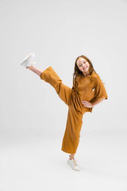 Küçük beyaz kızın tam boy portresi, gri stüdyo arka planında izole edilmiş hareket halinde çocuk pozu.