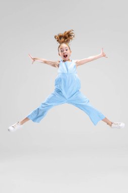 Gri arka planda izole edilmiş, küçük, neşeli bir kızın tam boy portresi.