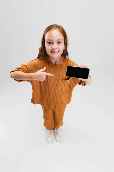 Retrato de vista superior da menina, criança apontando para a tela do telefone isolado sobre fundo cinza. Conceito de mídia social — Fotografia de Stock