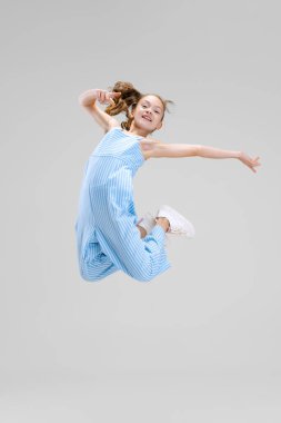 Gri arka planda izole edilmiş, küçük, neşeli bir kızın tam boy portresi.