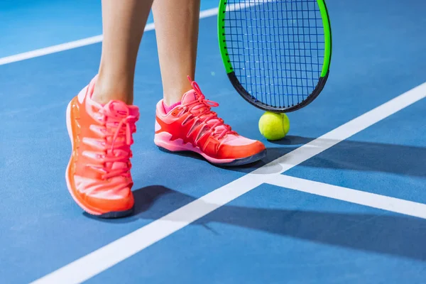Detailní záběr ženských nohou, sportovních tenisek a tenisové rakety s míčkem izolovaným přes kurt pozadí — Stock fotografie