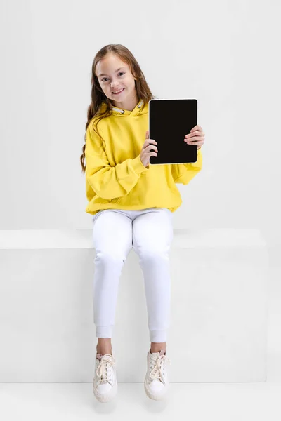 Portrait of little Caucasian girl, child pointing at tablet isolated over white studio background. Social networks — Stock Photo, Image