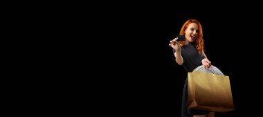 Elinde kredi kartı olan heyecanlı bir kadın siyah arka planda izole edilmiş. İnternetten alışveriş, satış. El ilanı