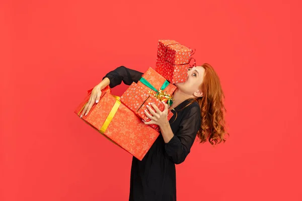 Vágott portré gyönyörű vörös hajú nő kezében sok ajándék dobozok elszigetelt piros háttér. Üdülési bevásárlás — Stock Fotó