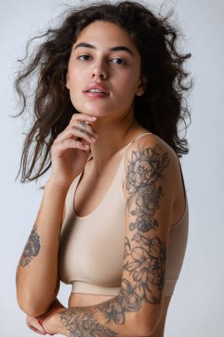 Kıvırcık saçlı, doğal makyajlı, gri stüdyo arka planında izole edilmiş güzel bir kadın portresi..