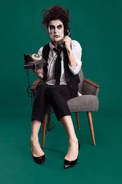 Mujer espeluznante, espeluznante en traje femenino blanco y negro con maquillaje loco y cabello desordenado sosteniendo teléfono vintage aislado sobre fondo verde — Foto de Stock
