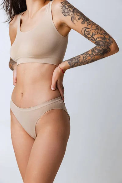 Cropped portrait of tender slim tanned female body in beige inner wear isolated over gray background. — Stock Photo, Image