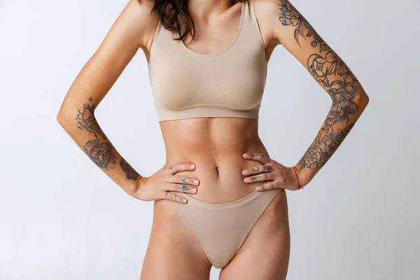 Vágott portré gyengéd karcsú cserzett női test bézs belső kopás elszigetelt szürke háttér. Sportos test — Stock Fotó