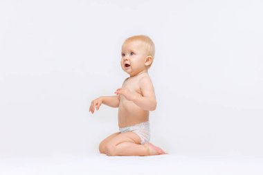 Küçük tatlı bir kızın tam boy portresi bebek bezi içinde sakince oturuyor ve beyaz stüdyo arka planında soyutlanmış bir şekilde oynuyor. Merak ettim.