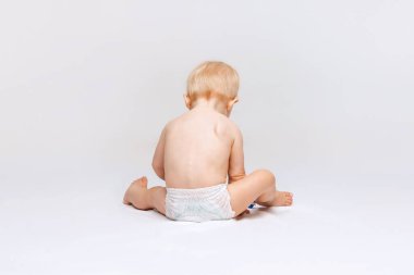 Küçük tatlı bir kızın arka plan portresi, bebek bezi içinde sakince oturuyor ve beyaz stüdyo arka planında soyutlanmış bir şekilde oynuyor..