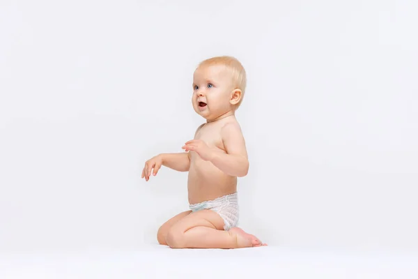 Retrato de cuerpo entero de una niñita linda, bebé sentado tranquilamente en pañal y jugando aislado sobre fondo blanco del estudio. Curioso. — Foto de Stock