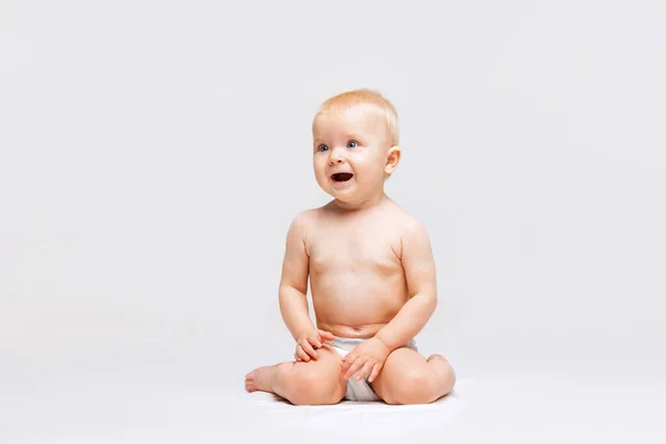 Retrato de cuerpo entero de una niñita linda, bebé sentado tranquilamente en pañal y jugando aislado sobre fondo blanco del estudio. Curioso. — Foto de Stock