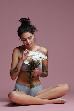 Gri iç çamaşırlı, beyaz çiçekli güzel bir kadının pembe arka planda izole edilmiş portresi.