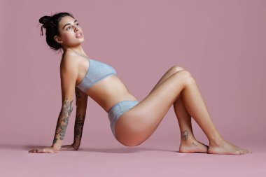 Pembe arka planda gri pamuklu iç çamaşırlı genç bir kadının tam boy yatay portresi..