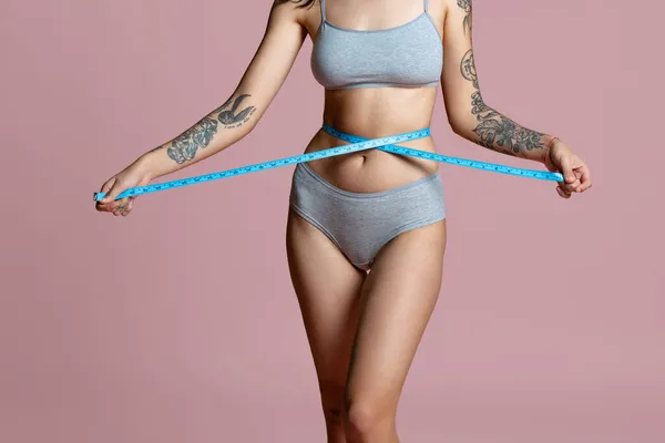 Retrato recortado de belo corpo feminino em cinza desgaste interno, medindo a cintura isolada sobre fundo rosa. Positividade do corpo — Fotografia de Stock