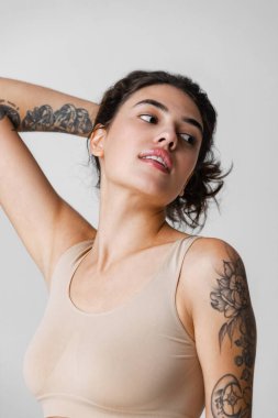 Saçları at kuyruklu, bej rengi iç çamaşırlarıyla doğal makyajlı, gri arka planda saklanmış güzel bir kadının kesilmiş portresi.