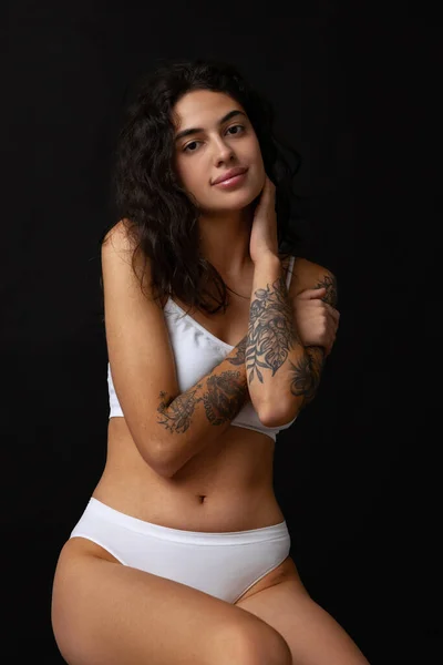 Cropped portrait of beautiful slim girl in white cotton underwear posing on chair isolated over dark background — Stock Photo, Image