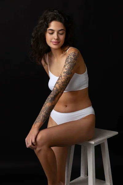 Cropped portrait of beautiful girl in white cotton underwear posing on chair isolated over dark background. Body positivity concept — Stock Photo, Image