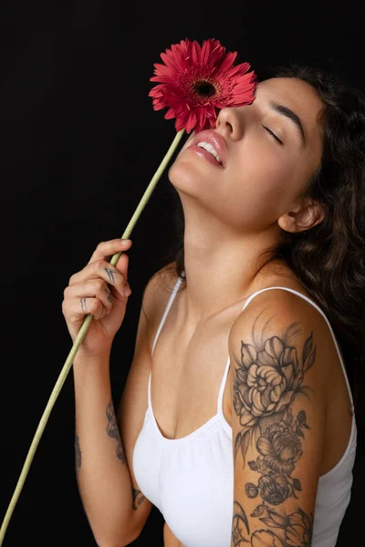 Cropped close-up portrait of beautiful tender woman with red gerberas posing isolated over dark background — Stock Photo, Image