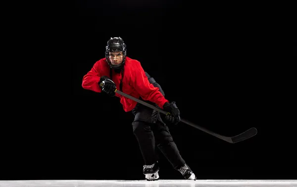 Full-length portrait of professional female hockey player training, dribbling puck isolated over black background. — Stock Photo, Image