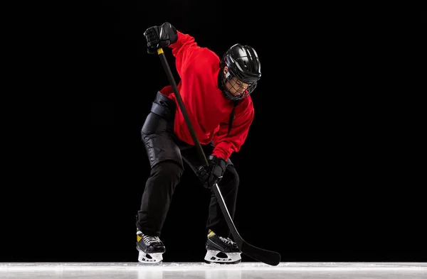 Full-length portrait of professional female hockey player training, dribbling puck isolated over black background.