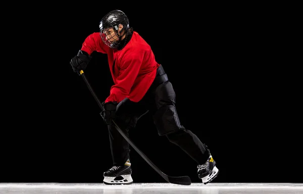 Full-length portrait of professional female hockey player training isolated over black background. Stickhandling