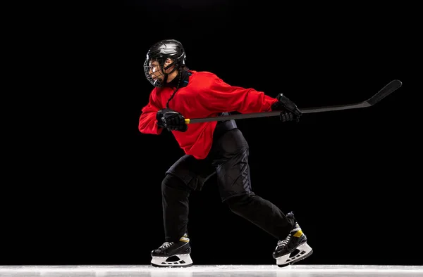 Full-length side view portrait of woman, professional hockey player in motion, training isolated over black background. High sticking game