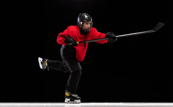 Full-length side view portrait of woman, professional hockey player in motion, training isolated over black background. High concentration