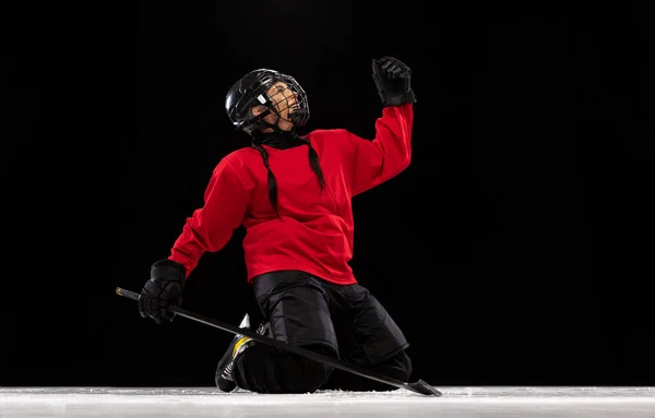 Portrait of professional female hockey player in special protective helmet isolated over black background. High motivation