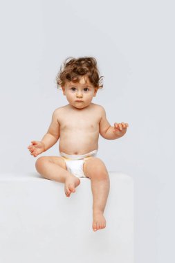 Tatlı çocuk, bebek. Küçük tatlı bir çocuğun portresi, bebek bezli bebek oturuyor, beyaz stüdyo arka planında izole edilmiş dudakları somurtuyor. Çocukluk kavramı, annelik, yaşam, doğum. İlan için alanı kopyala