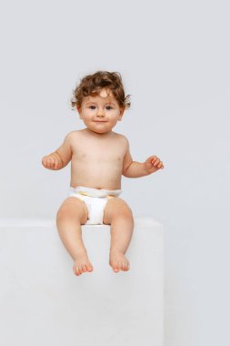 Sevimli, sevimli çocuk. Küçük tatlı bir çocuğun portresi, bebek bezi içindeki bebek sakince beyaz stüdyo arka planında izole bir şekilde oturuyor. Çocukluk kavramı, annelik, yaşam, doğum. İlan için alanı kopyala