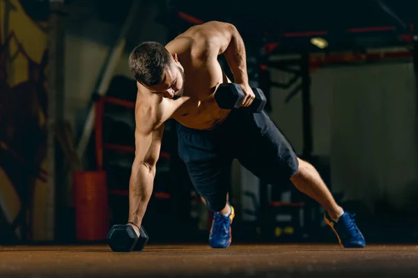 Полнометражный портрет спортивного мужчины, делающего отжимания с гантелями, тренирующегося в спортзале — стоковое фото