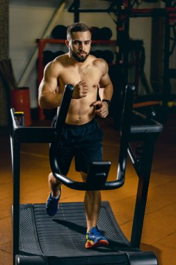 Koşu bandında kardiyo yapan genç bir adamın tam boy portresi. Beden eğitimi.