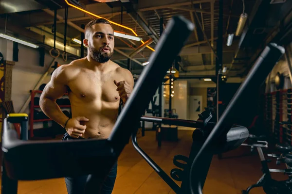 Cropped portrait of young sportive man running on a treadmill. Doing cardio.