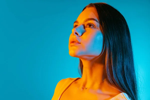 Retrato de una joven hermosa mirando hacia otro lado, posando aislada sobre fondo azul en luz de neón —  Fotos de Stock