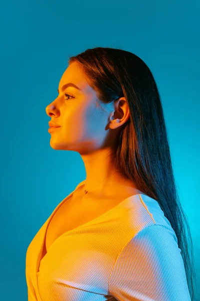 Vista laterale ritratto di giovane bella ragazza guardando lontano isolato su sfondo blu in luce al neon — Foto Stock