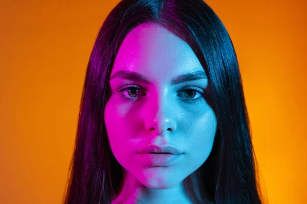 Ritratto ravvicinato della giovane ragazza che guarda la fotocamera isolata su sfondo arancione in luce al neon — Foto Stock