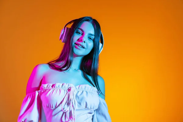 Обрізаний портрет молодої красивої дівчини, що слухає музику в навушниках ізольовано на помаранчевому фоні в неоновому світлі — стокове фото