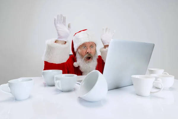 Ausgeschnittenes Porträt eines älteren Mannes im Weihnachtsmannkostüm, der am Schreibtisch voller leerer Kaffeetassen sitzt und auf Laptop schaut — Stockfoto