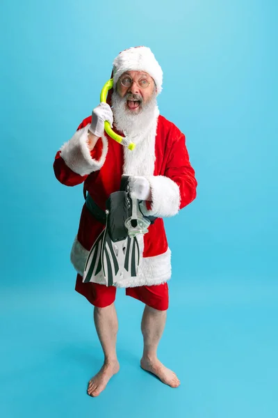 Ganztägiges Porträt eines fröhlichen älteren Mannes im Weihnachtsmannkostüm, Taucherbrille und Flossen isoliert vor blauem Hintergrund — Stockfoto