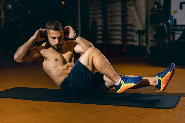 Retrato del hombre deportivo haciendo abdominales en la alfombra del gimnasio, construyendo seis paquetes abdominales — Foto de Stock