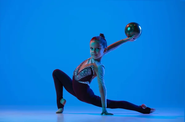 女の子の完全な長さの肖像画,プロのリズミカルな体操トレーニング,ネオンで青の背景に隔離されたピンクのボールで実行 — ストック写真