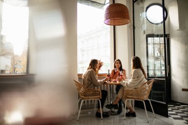 Kafede oturup kırmızı şarap içen üç güzel kadının tam boy görüntüsü.