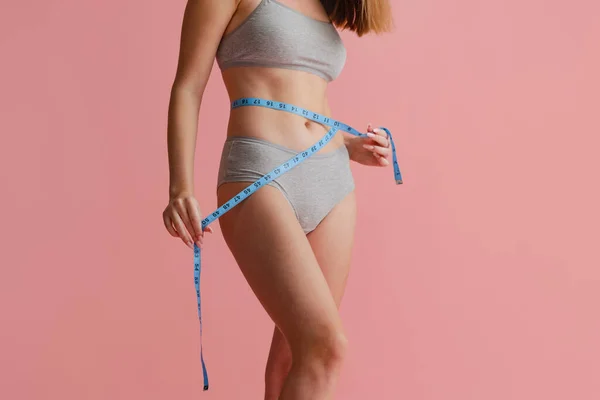 Retrato recortado de hermoso cuerpo femenino natural en desgaste interior gris, midiendo la cintura aislada sobre fondo rosa. Positividad corporal —  Fotos de Stock