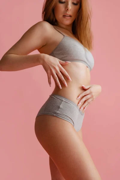 Cropped side view portrait of beautiful young woman in gray underwear posing isolated over pink background. — Stock Photo, Image
