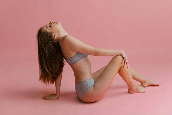 Retrato horizontal de larga duración de una joven atractiva posando en ropa interior gris aislada sobre fondo rosa. —  Fotos de Stock