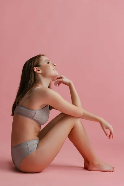 Retrato vertical de larga duración de una joven atractiva posando en ropa interior gris aislada sobre fondo rosa. — Foto de Stock